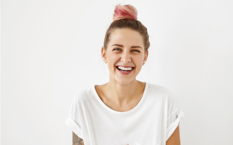 girl laughing with tattoo on arm and pink hair in bun